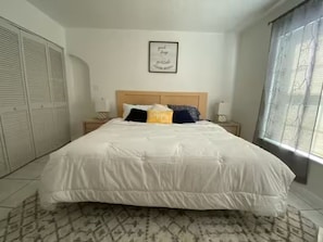 Un dormitorio con una cama grande, cabecero, mesita de noche, lámpara de pared y cortinas.