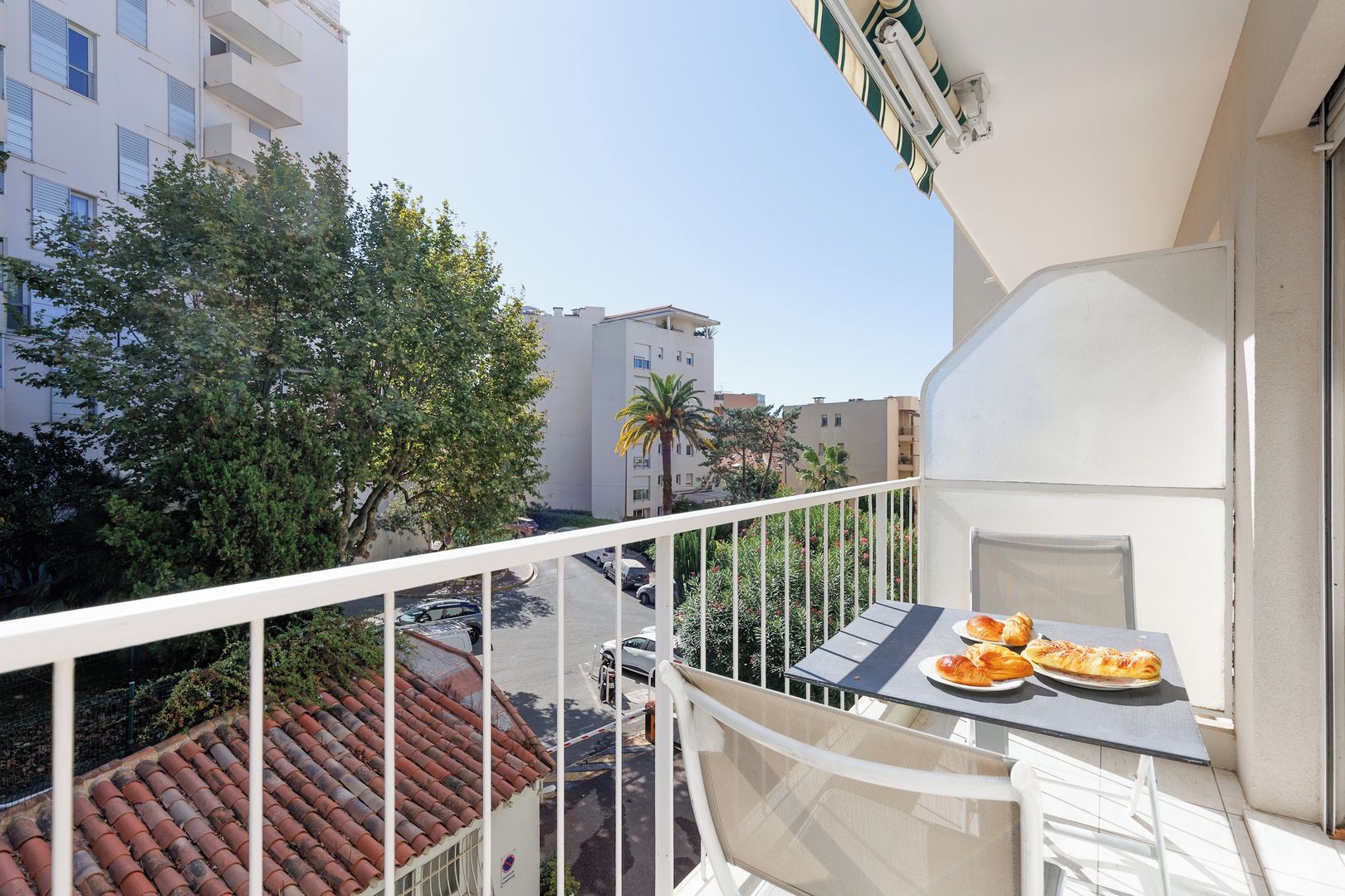 A balcony with a table set for two, overlooking a street with parked cars and buildings.