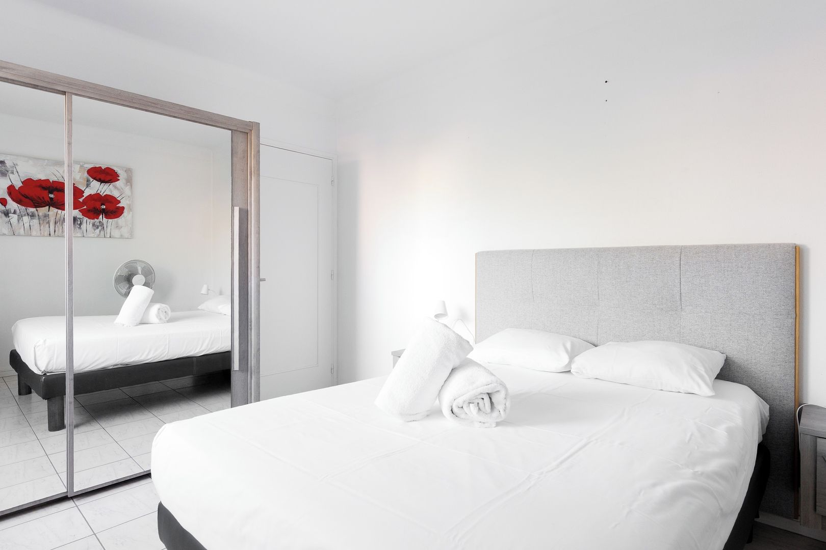A hotel room with a bed, a bedside table, a mirror, and a door leading to another room.