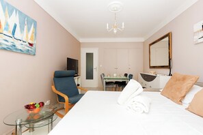Ein Hotelzimmer mit Bett, Schreibtisch, Stuhl, Fernseher, Esstisch und einem Gemälde.