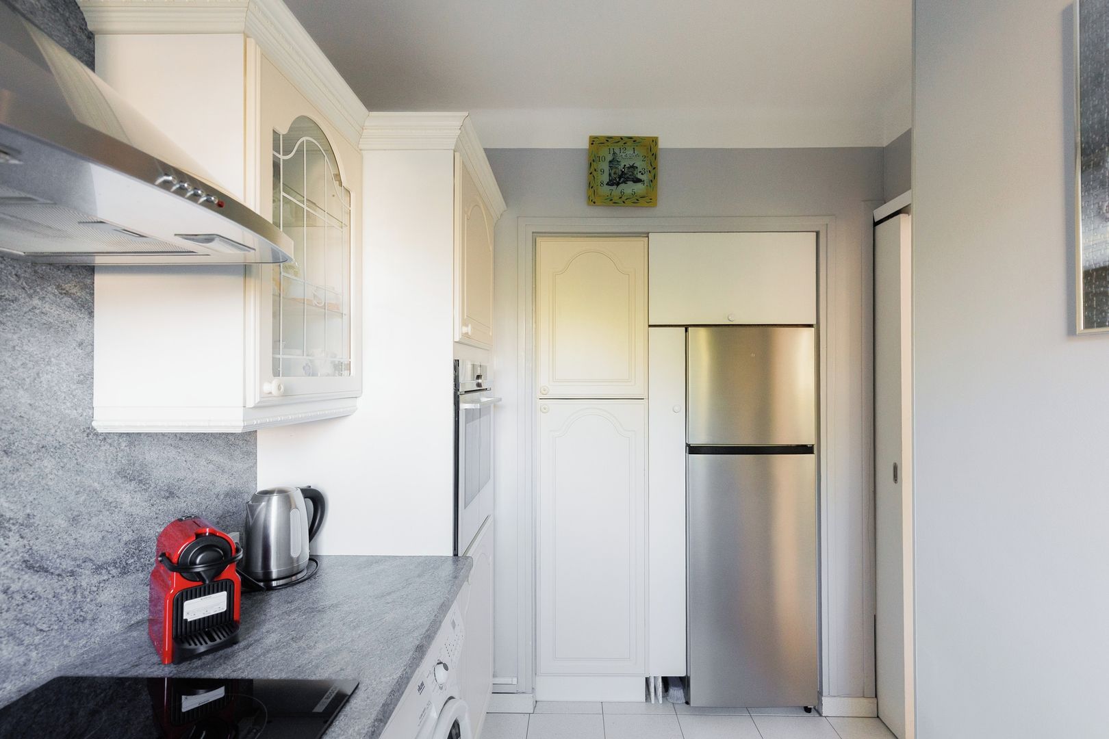 Cocina compacta con refrigerador de acero inoxidable, horno empotrado y cafetera sobre la encimera.