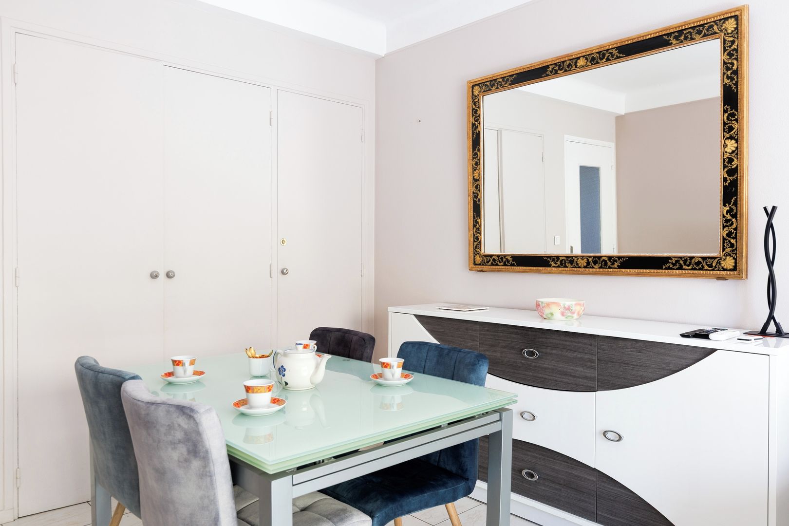 A dining area with a glass table, chairs, and a white cabinet with a mirror.