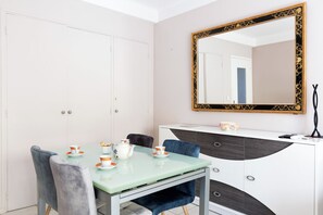 A dining area with a glass table, chairs, and a white cabinet with a mirror. - Upstays Cosy Calm 1 Bedroom with terrace and AC (Cannes)
