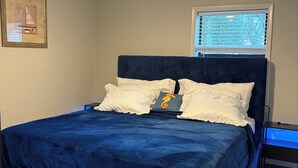 Una camera da letto con un letto, una ventola a soffitto, una finestra con persiane e un comodino con una lampada.
