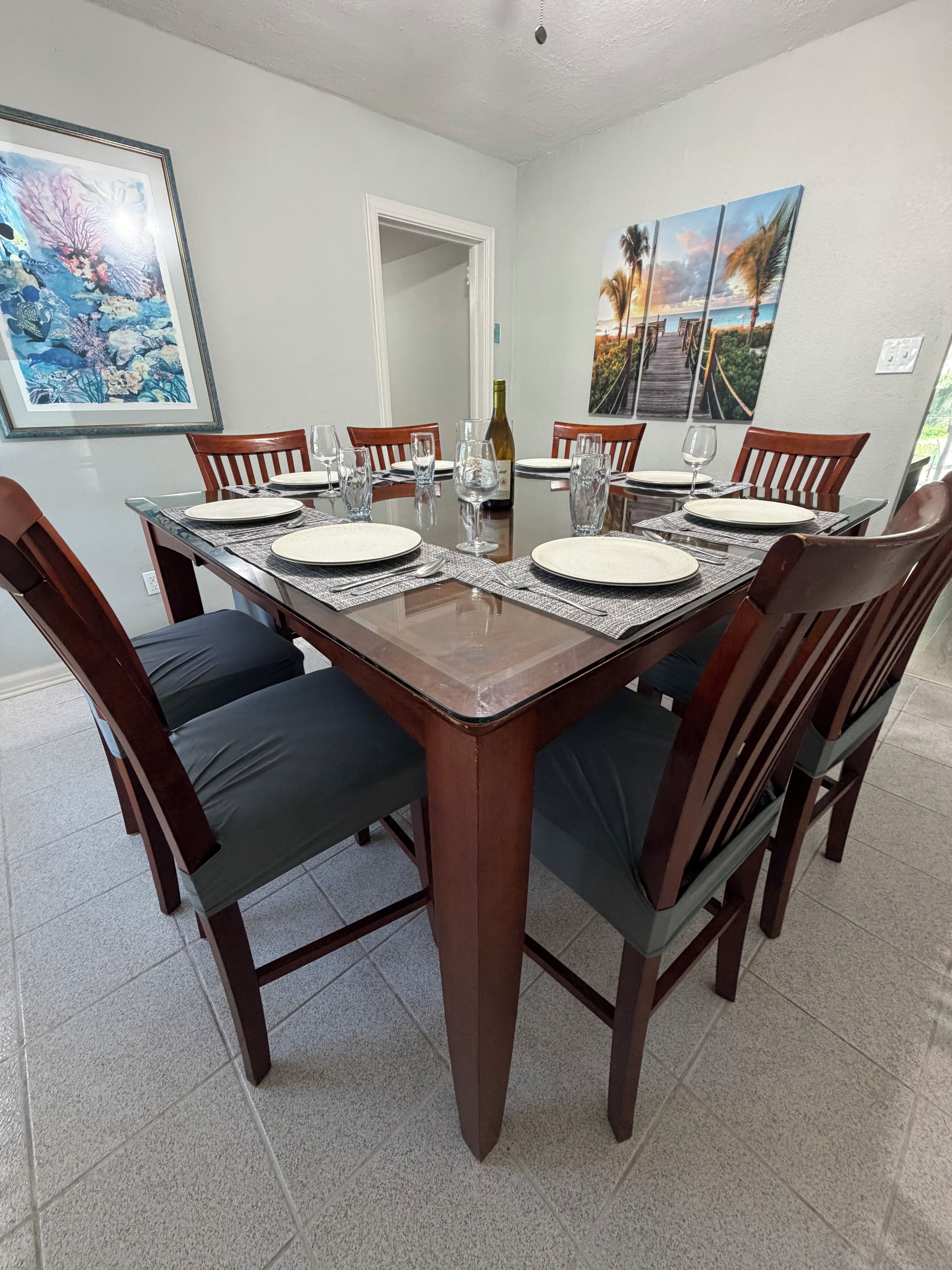 A dining room with a rectangular table set for six, surrounded by wooden chairs with cushioned seats.