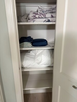 Ein Schrank mit Regalen, gefüllt mit gefalteter Kleidung und einem Kissen.