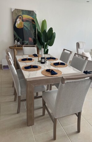 A dining table set with placemats, napkins, and a candle, surrounded by chairs with cushioned backs. - Sunset Balcony + El Yunque Views + 100" TV (Río Grande)