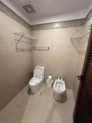 A bathroom with two toilets, a bidet, a towel rack, and a trash bin. - Sunset Balcony + El Yunque Views + 100" TV (Río Grande)