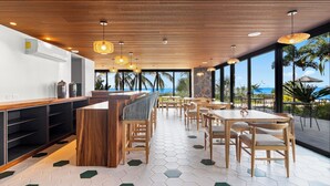 A modern restaurant with wooden furniture, hexagonal patterned flooring, and large windows offering a view of the ocean. - Cozy Modern Condo with Scenic Balcony Views (Bucerías)
