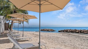 A beachside seating area with umbrellas and lounge chairs, a rocky shoreline, and a clear view of the sea. - Cozy Modern Condo with Scenic Balcony Views (Bucerías)
