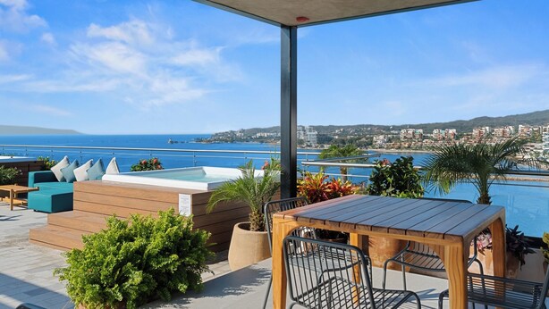 A terrace with a pool, seating area, and a view of the sea and buildings. - Cozy Modern Condo with Scenic Balcony Views (Bucerías)