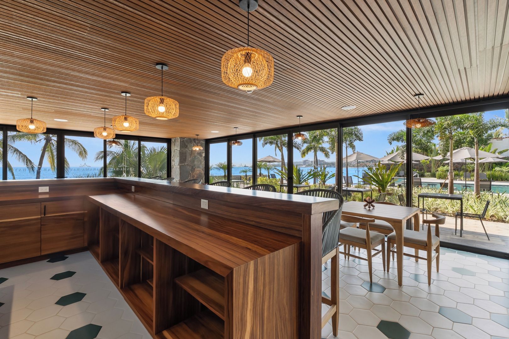 Un área de bar moderna con mostrador de madera, luces colgantes y vista al océano.