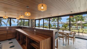 Un área de bar moderna con mostrador de madera, luces colgantes y vista al océano.