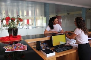 A reception desk with a computer, a vase with red flowers, and brochures. - Palace Hotel & SPA Termas DE SAO Tiago (Penamacor)