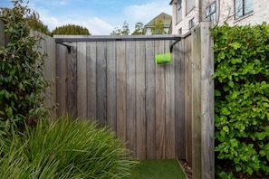 A wooden fence with a green hanging object, a grassy area, and a hedge. - Over The Moon | Quiet CBD w/ Courtyard (Christchurch)