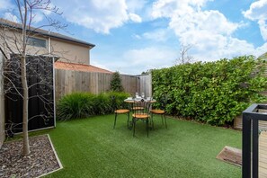 A backyard with a small table and chairs, surrounded by a wooden fence and a hedge. - Over The Moon | Quiet CBD w/ Courtyard (Christchurch)