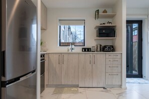 A modern kitchen with a stainless steel refrigerator, wooden cabinets, a window, and a countertop with various appliances. - Over The Moon | Quiet CBD w/ Courtyard (Christchurch)