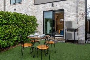 A patio with a table and chairs, a hedge, and an air conditioning unit. - Over The Moon | Quiet CBD w/ Courtyard (Christchurch)