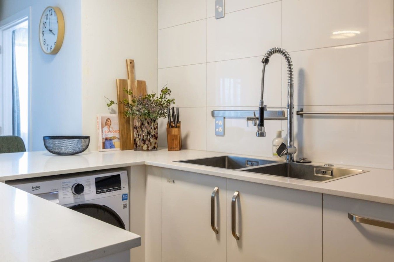 Una cocina moderna con lavadora integrada, lavamanos de acero inoxidable y un reloj en la pared.