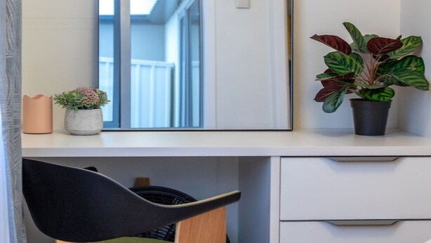 Un escritorio con espejo, una planta en maceta, un jarrón pequeño y una silla.