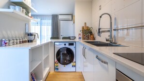 Una cocina compacta con lavadora integrada, un lavamanos y una cafetera.