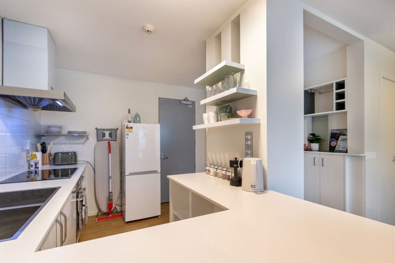 A modern kitchen with white cabinetry, a built-in oven, and a coffee machine.