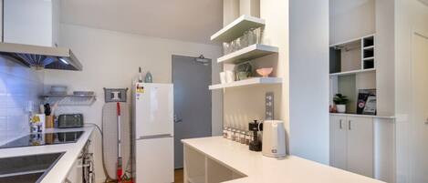 A modern kitchen with white cabinetry, a built-in oven, and a coffee machine.