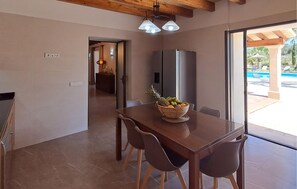 A dining area with a table, chairs, and a fruit bowl. There is a kitchen area with cabinets and a refrigerator in the background. - Awesome home in Felanitx with sauna (Felanitx)