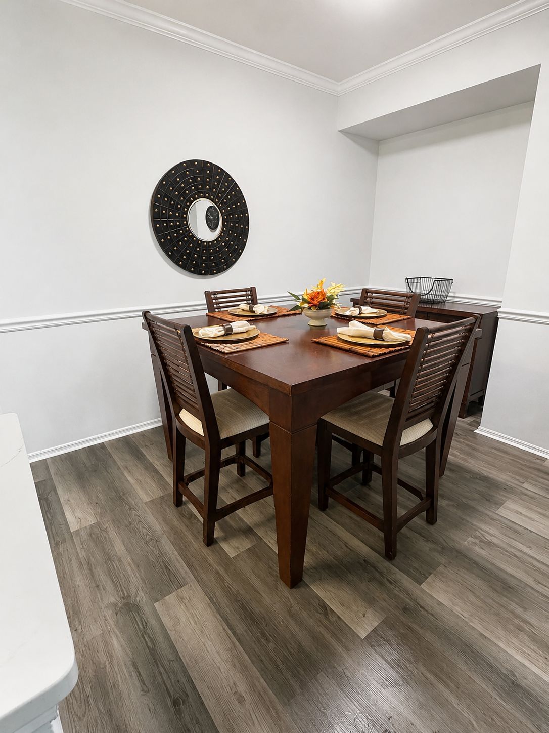A dining area with a round table, six chairs, and a wall-mounted decorative mirror.