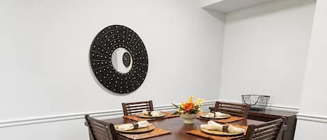 A dining area with a round table, six chairs, and a wall-mounted decorative mirror.