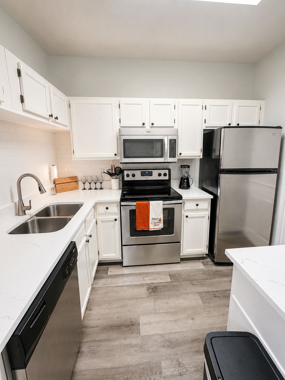 A modern kitchen with white cabinets, stainless steel appliances, and a wooden floor.