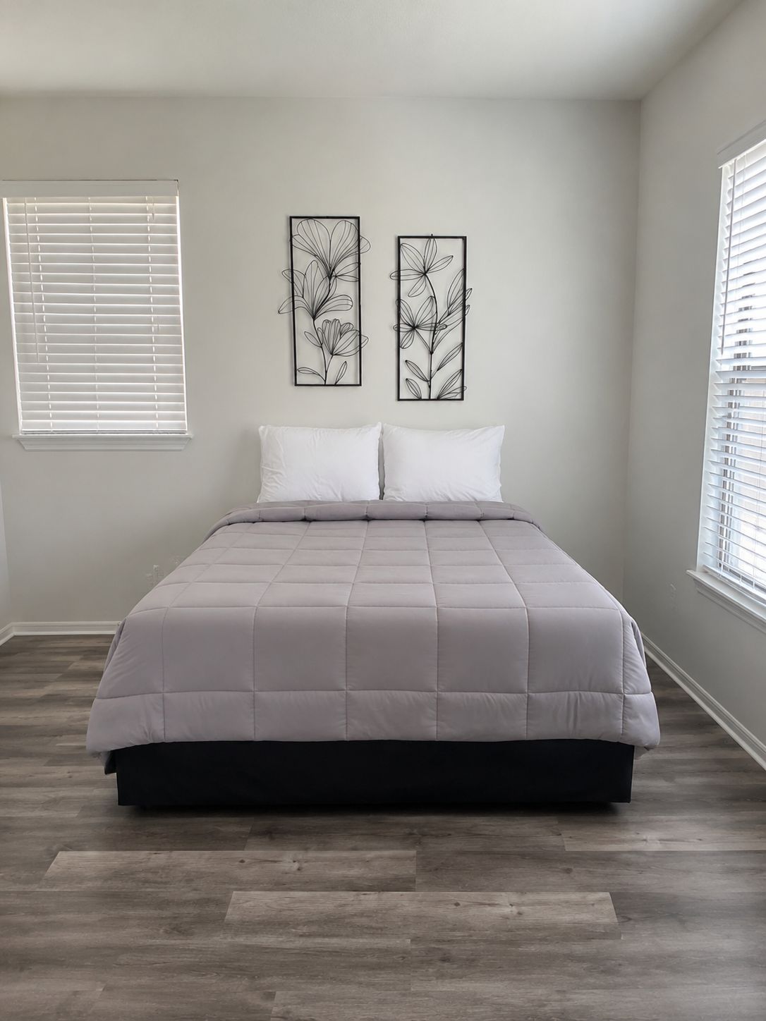 A bedroom with a bed, two wall-mounted artworks, and a window with blinds.
