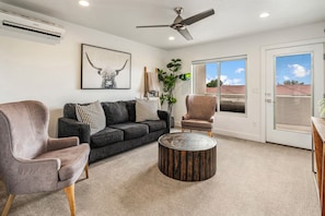 Ein Wohnzimmer mit grauem Sofa, zwei Sesseln, einem runden Couchtisch und einem Deckenventilator.