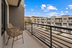 Ein Balkon mit Korbstuhl, Metallgeländer und Blick auf mehrstöckige Gebäude.