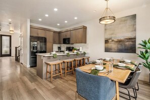 A modern kitchen with wooden cabinets, a central island with stools, and a dining area with a table set for four. - The Vue 5, Resort Pool, Private Balcony, Grill (Saint George)