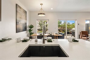 A modern kitchen with a central island, a dining area with a view, and a large window. - The Vue 5, Resort Pool, Private Balcony, Grill (Saint George)