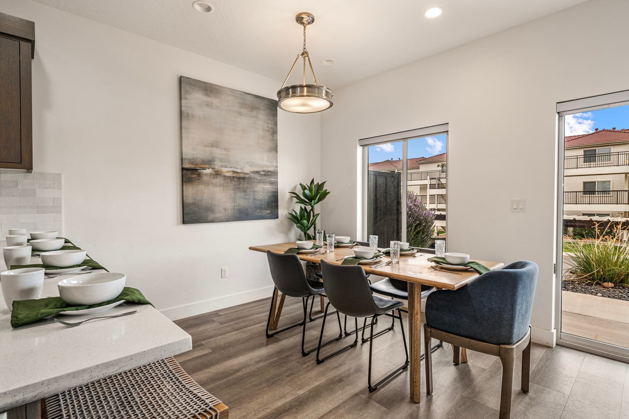 A modern kitchen with a dining area, large windows, and a view of the outside.
