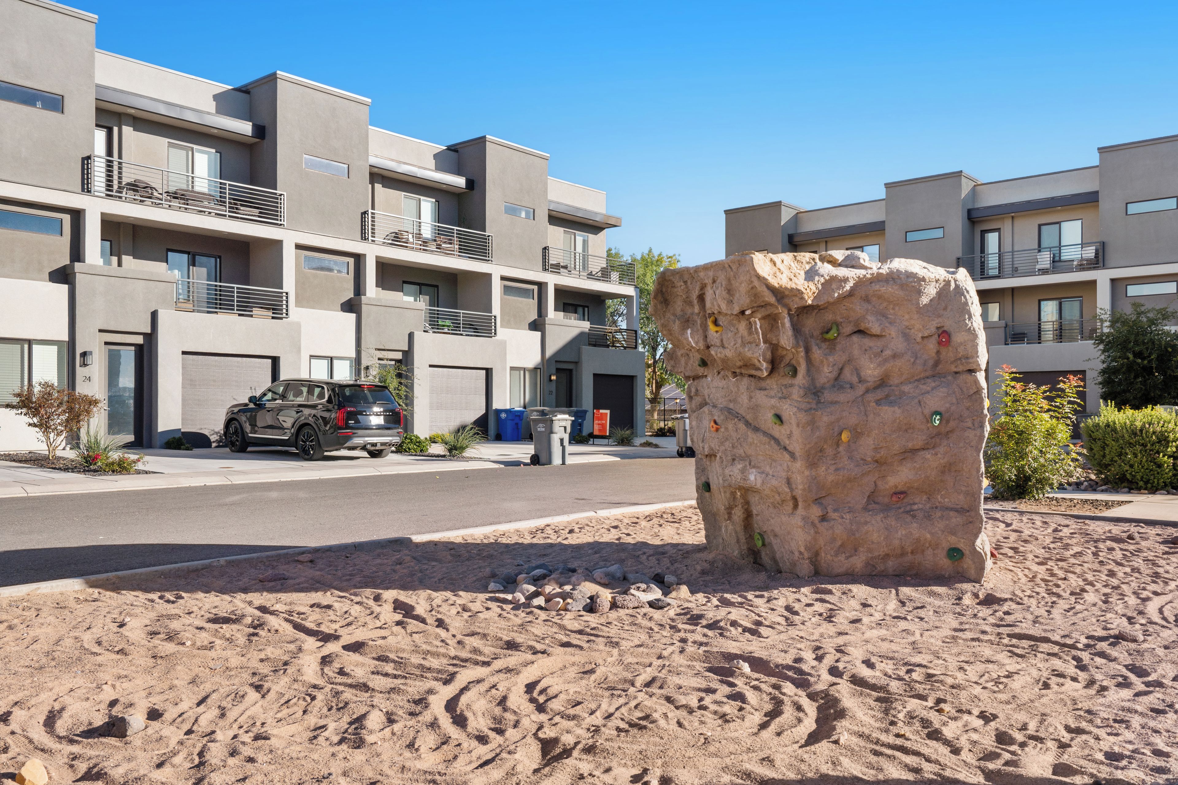 A modern apartment building with multiple balconies and a large rock sculpture in the foreground.