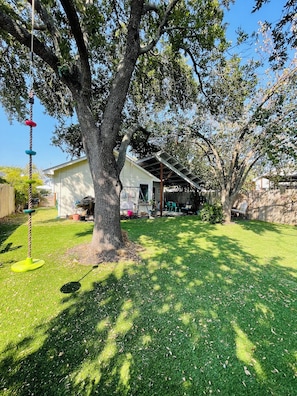 A backyard with a large tree, a play structure, and a covered patio area.
