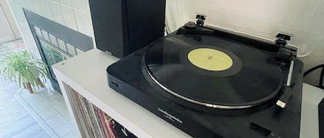 Um toca-discos numa prateleira branca, com um alto-falante e uma planta ao fundo.