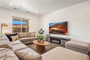 A modern living room with a sectional sofa, a fireplace, a large window, and a wall-mounted TV. - Skyline 1753, Private Hot Tub, Resort Amenities, and Close to Sand Hollow! (Washington)