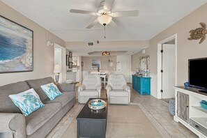 A living room with a ceiling fan, a television, a sofa with decorative pillows, a coffee table, and a dining area in the background. - Oceanfront Condominium with Great Amenities (St. Simons Island)