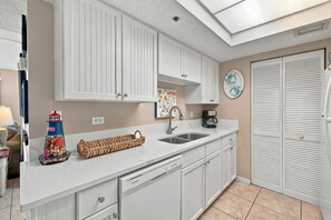 A kitchen with white cabinets, a sink, a coffee maker, and a decorative plate on the wall. - Oceanfront Condominium with Great Amenities (St. Simons Island)