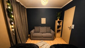 Une pièce avec un canapé gris, un meuble en bois, une porte et une plante.