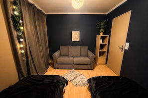Ein Zimmer mit einem grauen Sofa, einem Holzschrank, einer Tür und einer Pflanze.