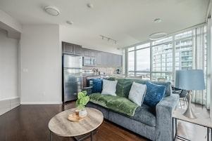 Uma sala de estar moderna com um sofá cinzento, uma mesa de centro de madeira e vista para o horizonte urbano através de grandes janelas.