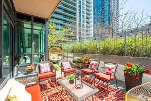 Una terraza en la azotea con mobiliario de mimbre, plantas en macetas y vistas de edificios circundantes.