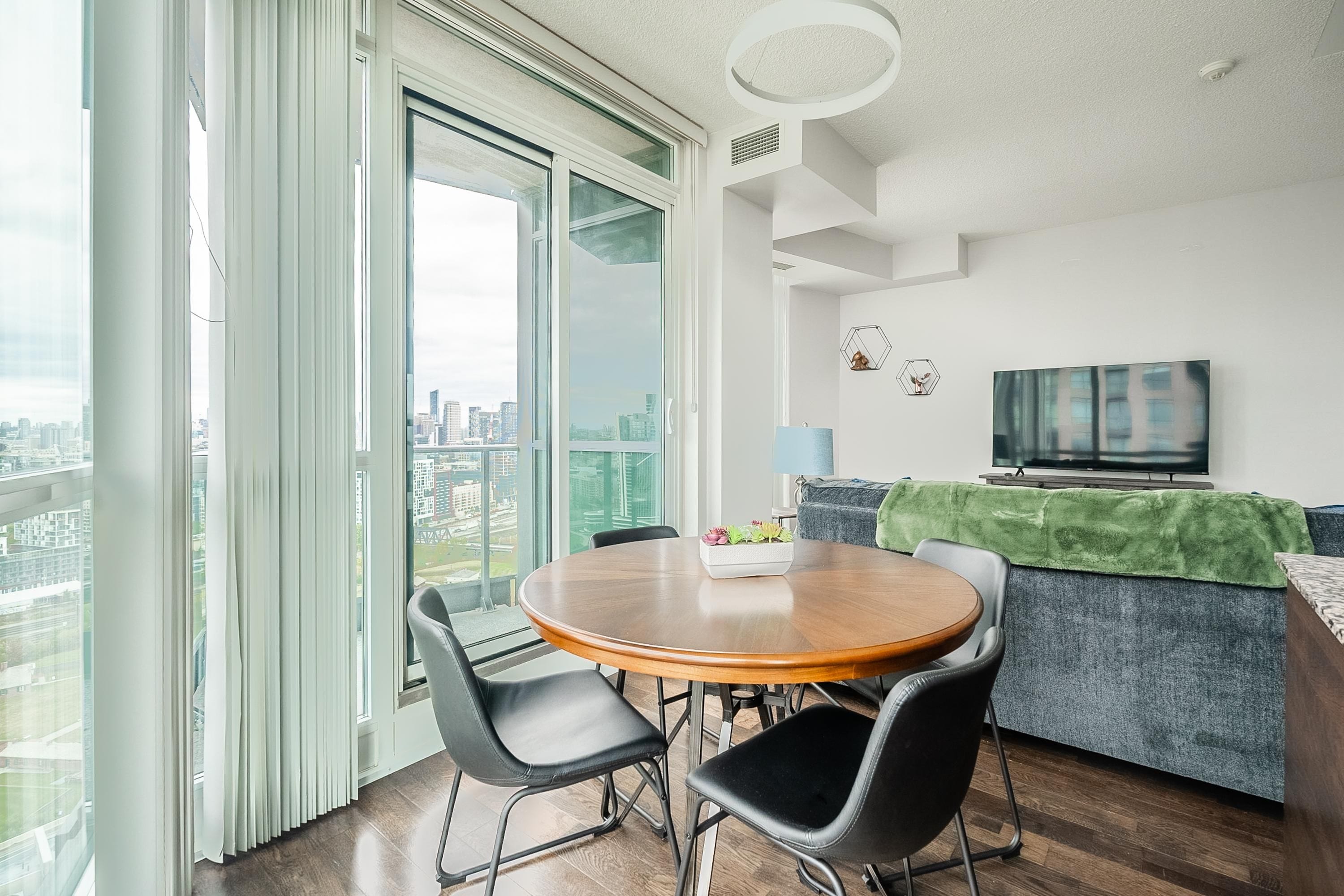 Een moderne woonkamer met een eettafel, stoelen, een bank, een televisie en uitzicht over de stad.