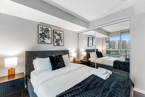A modern hotel room with a large bed, a nightstand with a lamp, a mirror, and artwork on the wall. - StayToronto - Fort York Downtown Suites (Toronto)