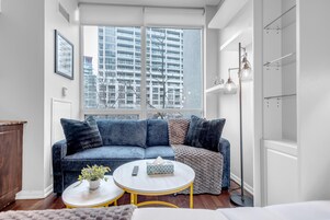 A modern living room with a blue sofa, a white round coffee table, and a large window with a city view.